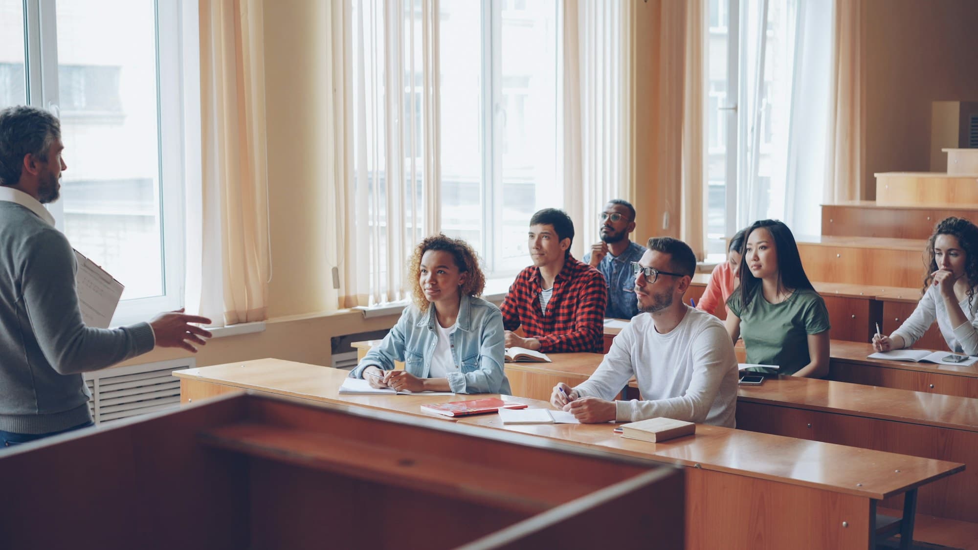 Young adults attentively listening to an instructor in a sunlit classroom